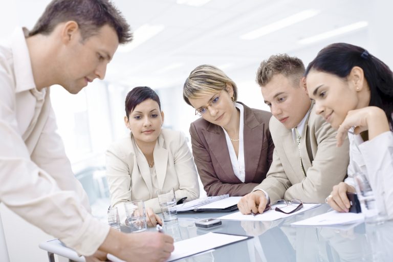 4 business people looking at a collegue's notepad as he jots down something