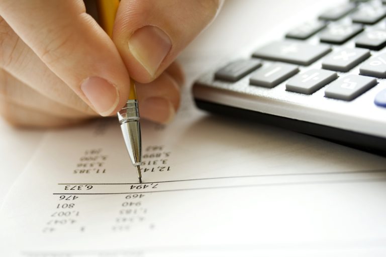 Close-up of a hand writing with a pen, next to a keyboard